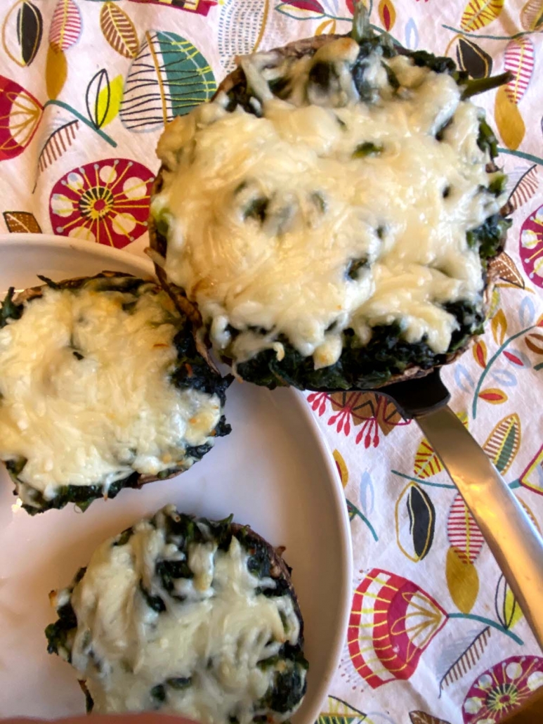 Close-up of spinach stuffed portobello mushroom topped with melted mozzarella cheese being lifted from the plate.