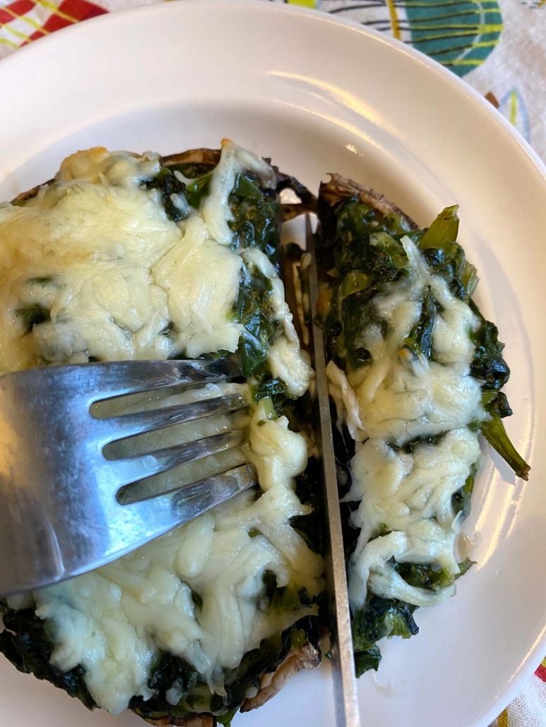 Close-up of spinach stuffed portobello mushroom being cut with a fork and knife.