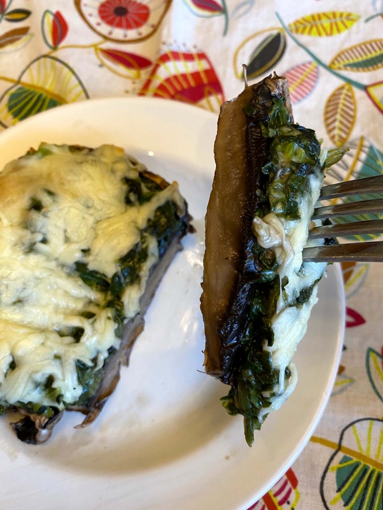 Slice of spinach stuffed portobello mushroom on a plate with melted cheese topping.