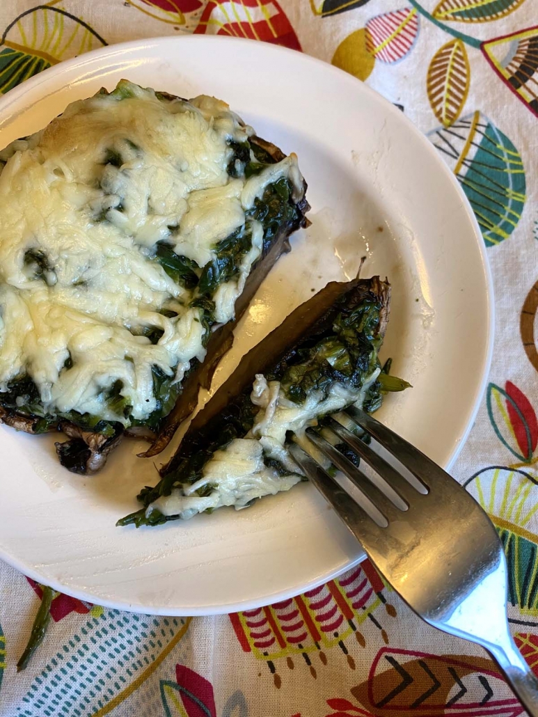 Spinach stuffed portobello mushroom cut in half on a plate with a fork, showing cheesy filling inside.