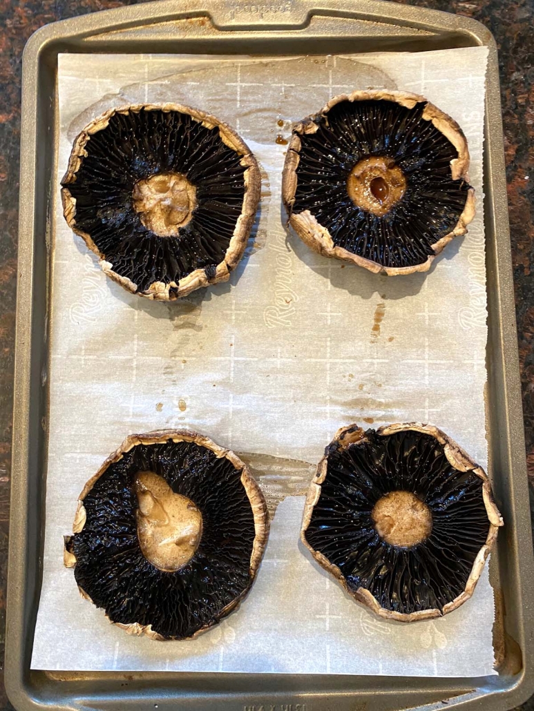 Portobello mushroom caps on a baking sheet lined with parchment paper ready to be stuffed with spinach and cheese.
