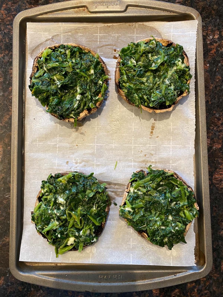 Portobello mushroom caps stuffed with spinach and Parmesan mixture on a baking sheet.