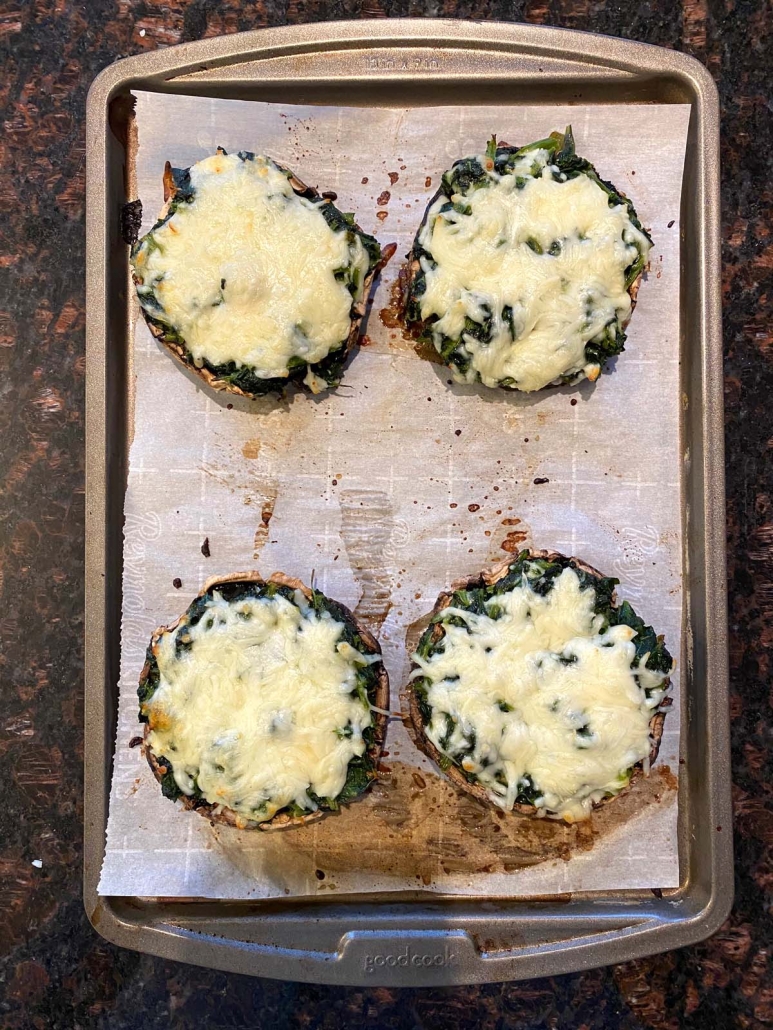Baked spinach stuffed portobello mushrooms fresh out of the oven with melted golden mozzarella cheese on top.