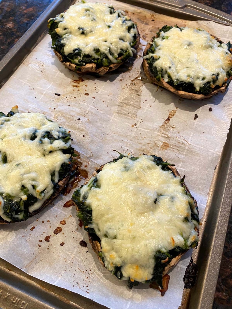 Cheesy spinach stuffed portobello mushrooms just baked in the oven on a parchment-lined sheet pan.
