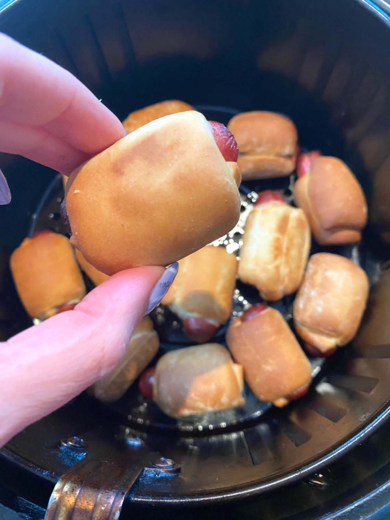 hand holding 1 bagel dog over air fryer with more bagel dogs
