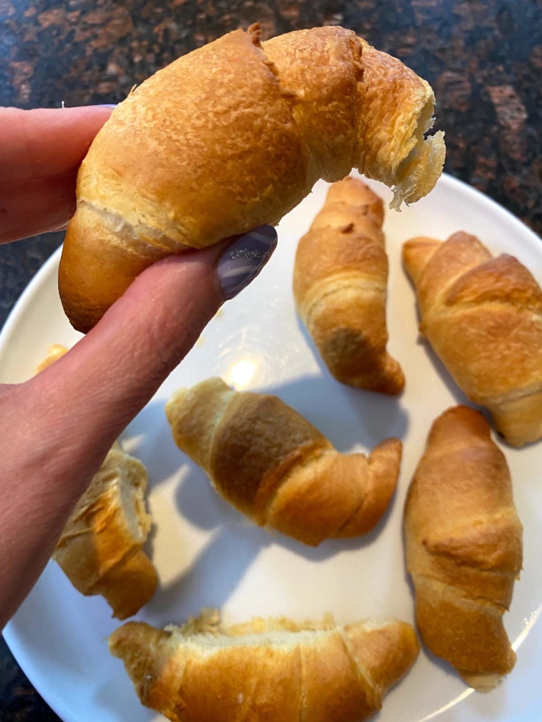 Hand holding crescent roll above plate