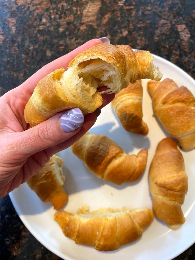 hand holding crescent roll above plate