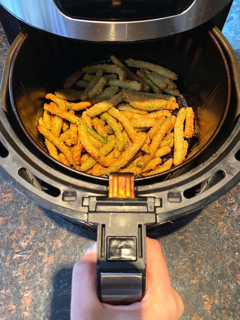 hand holding air fryer basket with breaded green beans