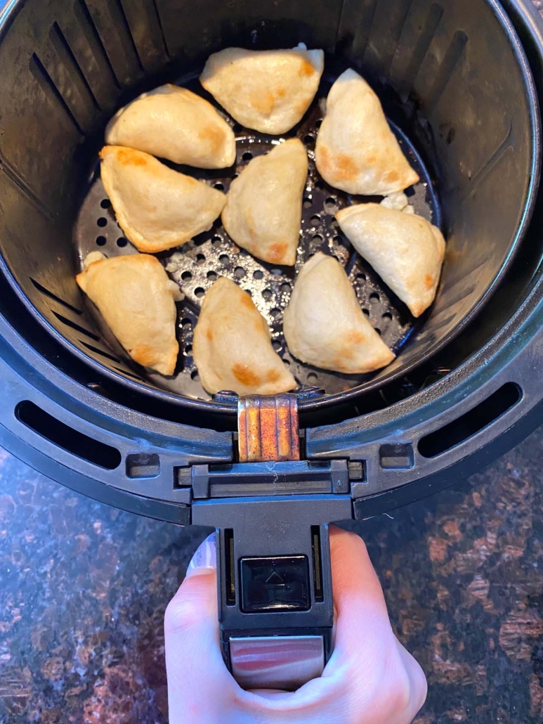 hand holding air fryer basket with pierogies