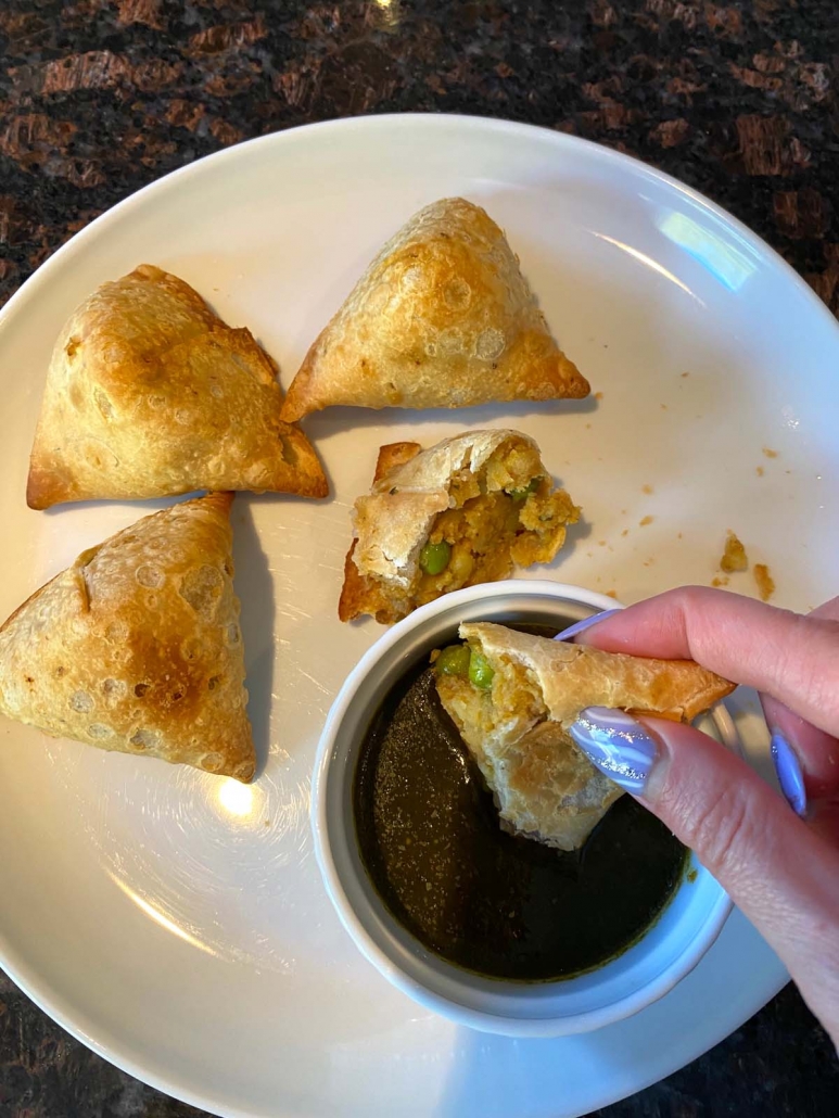 Crispy cooked samosas on plate and being dipped in sauce