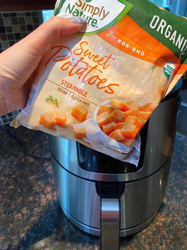 hand holding bag of frozen sweet potatoes in front of air fryer