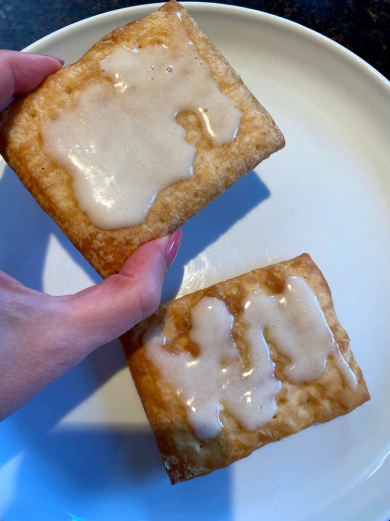 toaster strudel with icing held in hand over plate