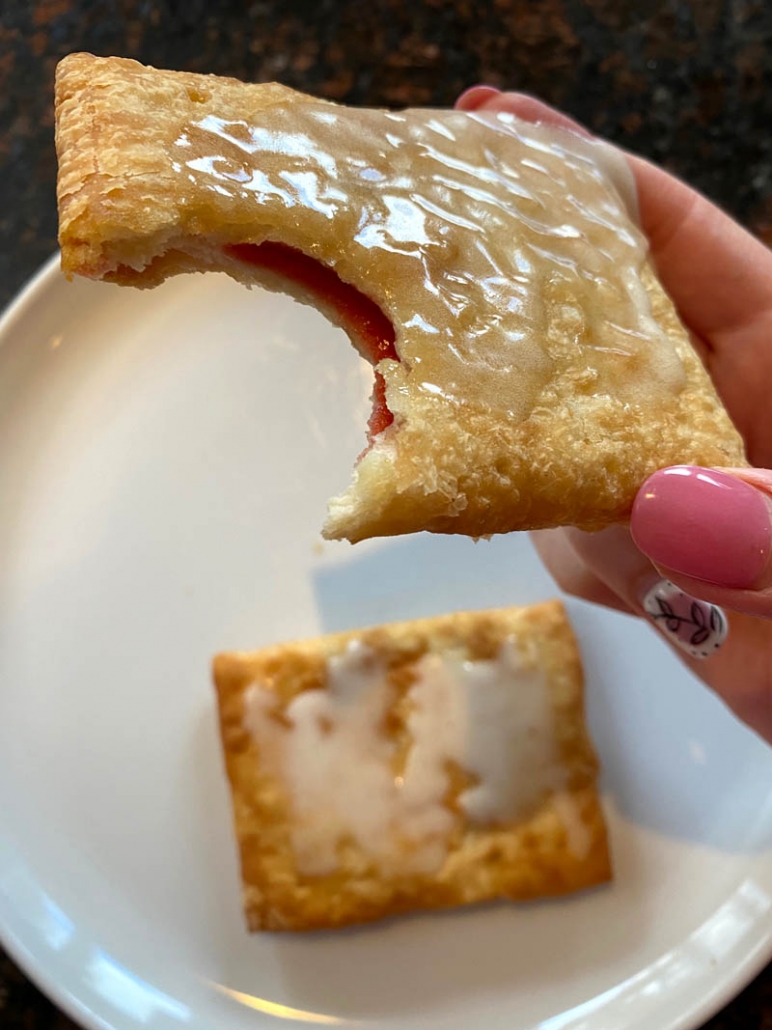 partially eaten toaster strudel held in hand over plate with toaster strudel