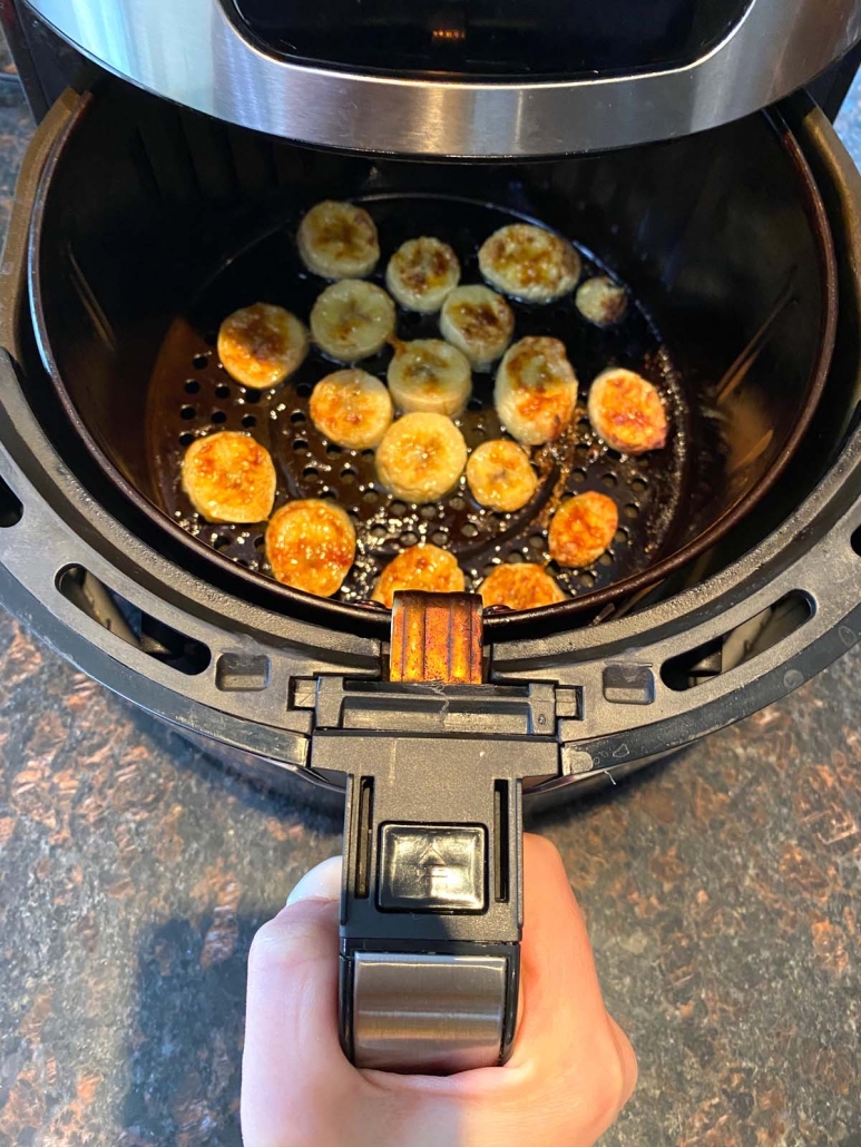 hand holding air fryer basket with banana slices