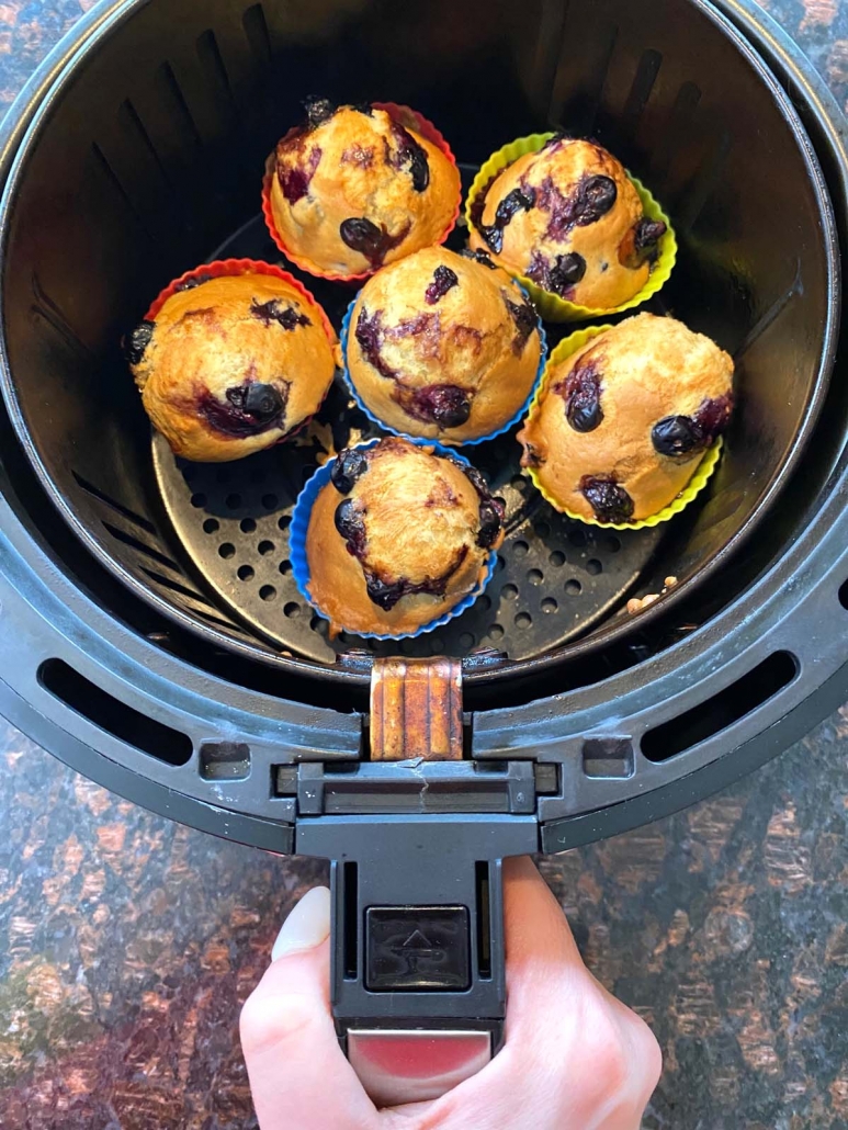 hand holding air fryer basket with blueberry muffins inside