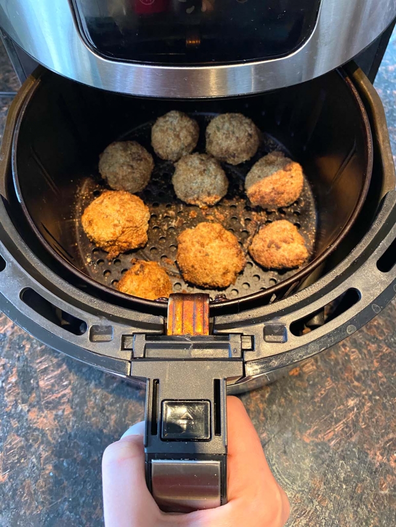 hand holding air fryer basket with breaded mushrooms