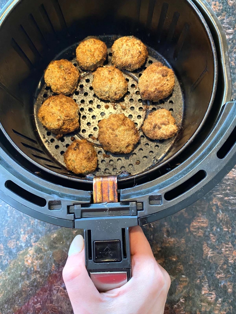 hand holding air fryer basket with breaded mushrooms