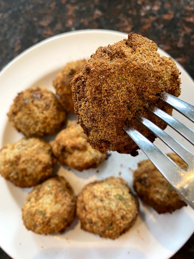 fork holding air fryer mushrooms above plate of breaded mushrooms