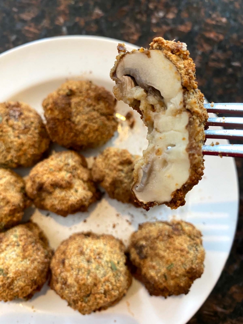 fork stabbing mushroom above plate of breaded mushrooms