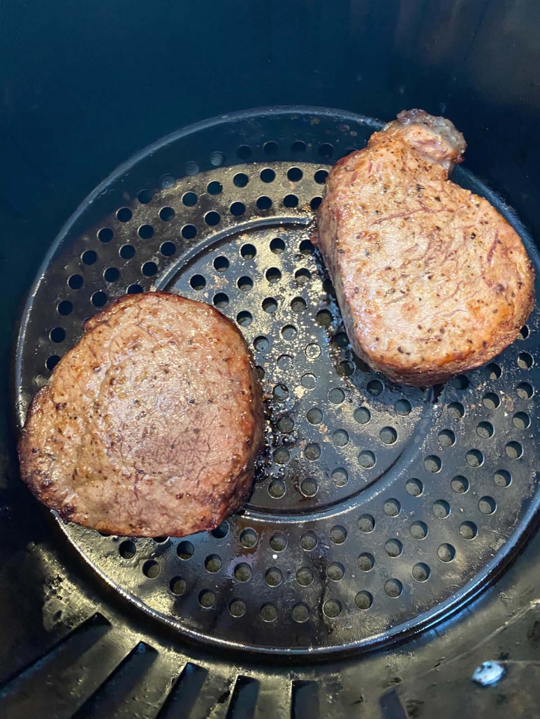 close up of two cooked filet mignon steaks in the air fryer basket