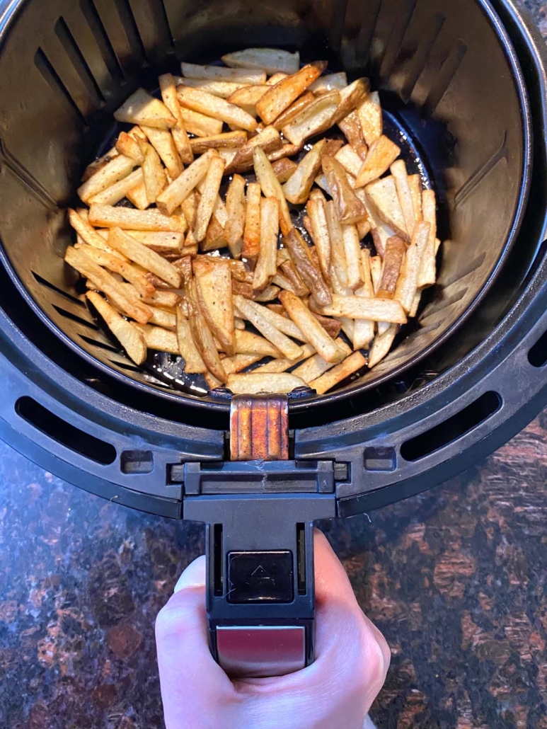 hand holding air fryer basket with french fries