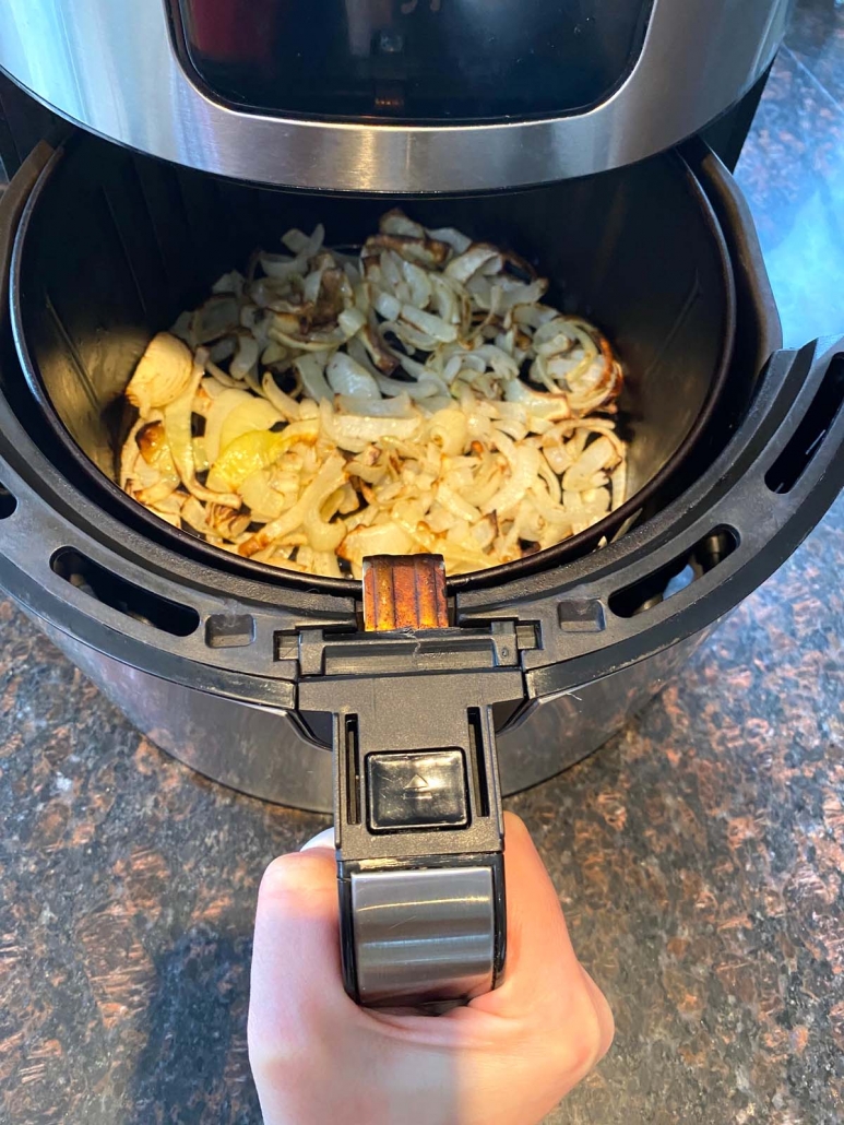 hand holding air fryer basket with fried onions inside