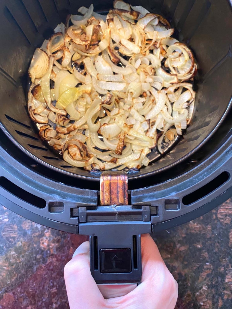 hand pulling out air fryer basket with fried onions inside