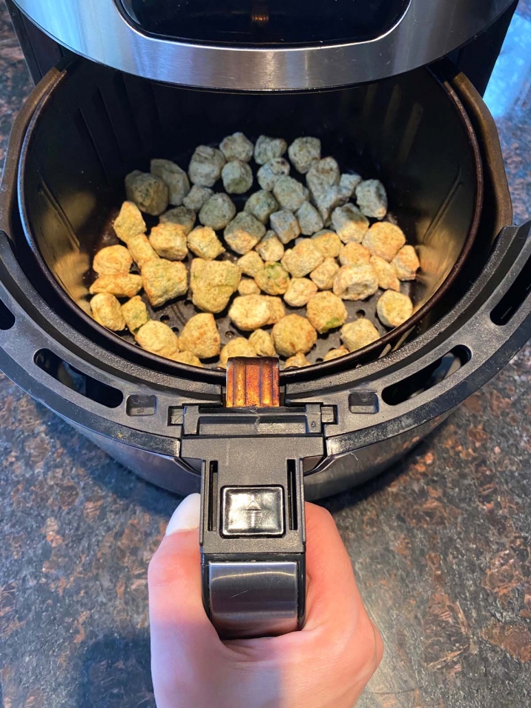 hand holding air fryer basket filled with frozen breaded okra pieces