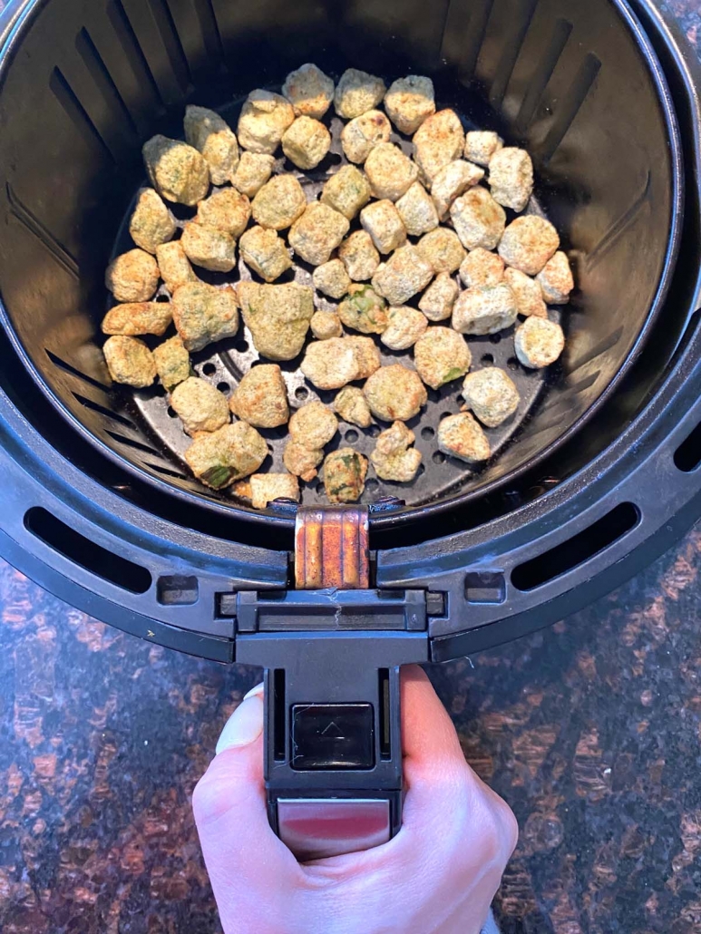 hand holding air fryer basket with frozen breaded okra inside