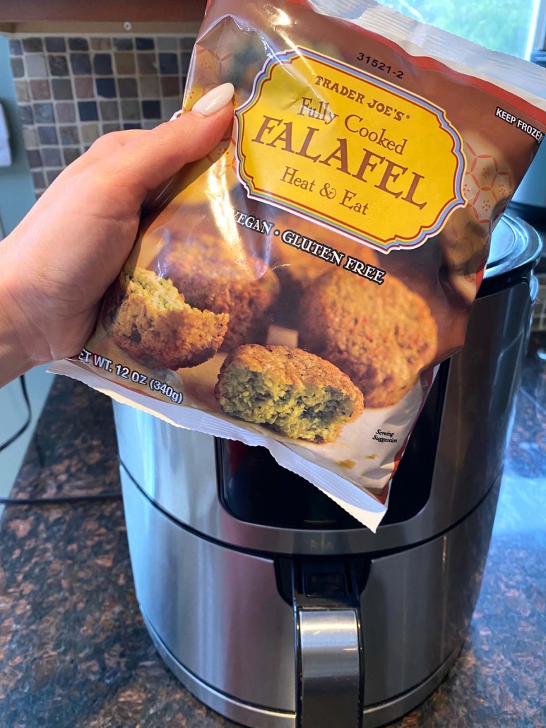 hand holding bag of frozen falafel in front of air fryer