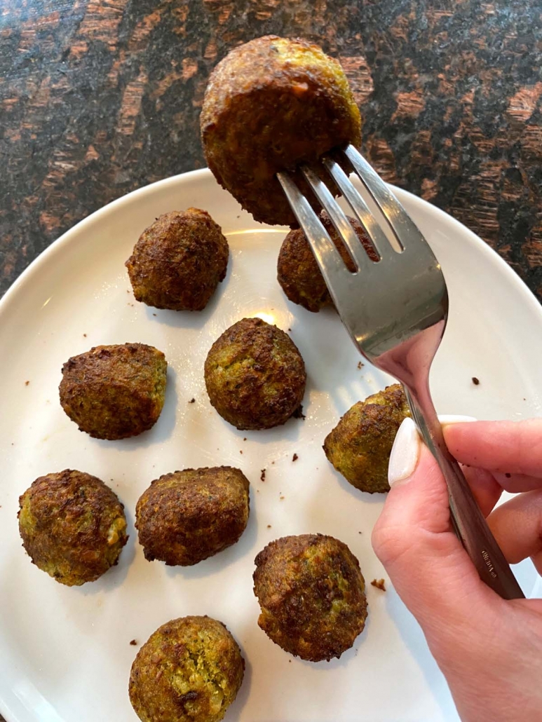 hand holding fork with falafel above plate of falafel