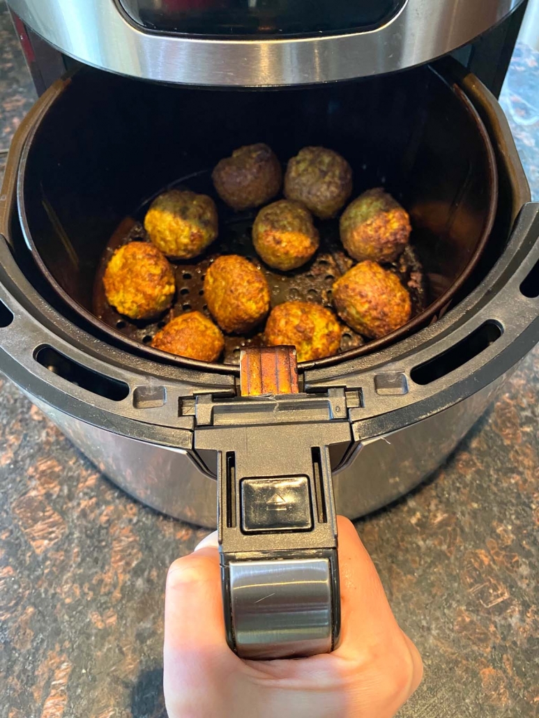 hand holding air fryer basket filled with frozen falafel