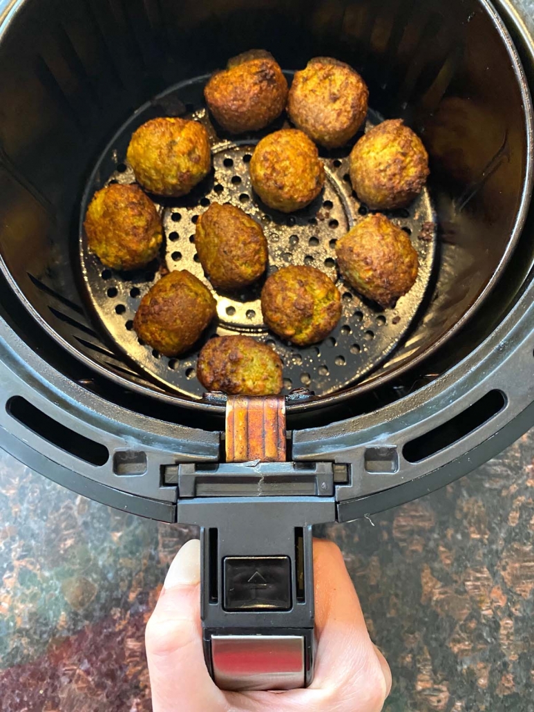 hand holding air fryer basket with frozen falafel