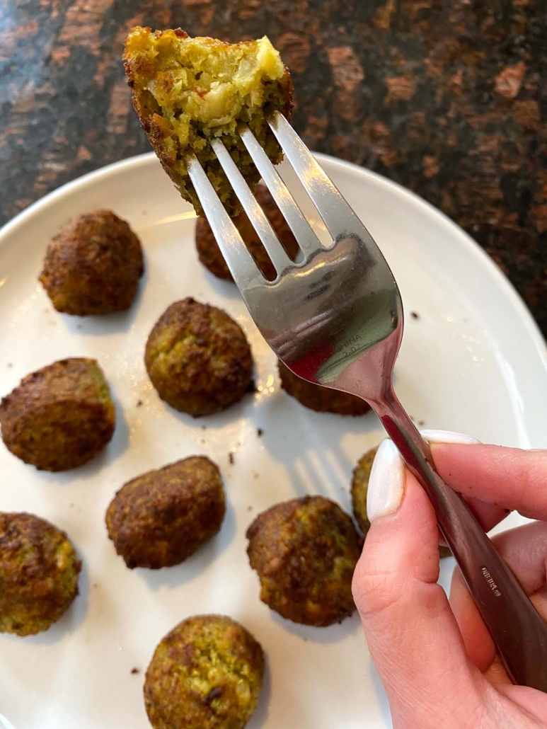 fork holding falafel above plate with falafel