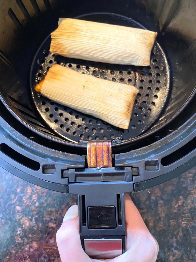 hand holding air fryer basket with tamales inside