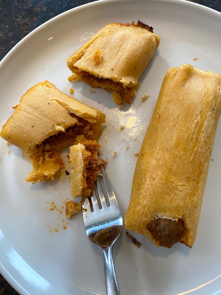 fork breaking apart cooked beef tamale on a white plate next to another tamale