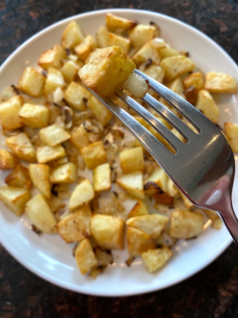 fork holding onion and potato pieces above plate of onions and potatoes