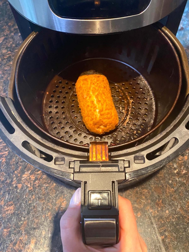 hand holding air fryer basket with chicken kiev inside