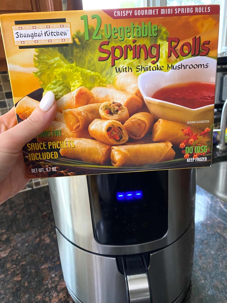 hand holding package of frozen spring rolls in front of air fryer
