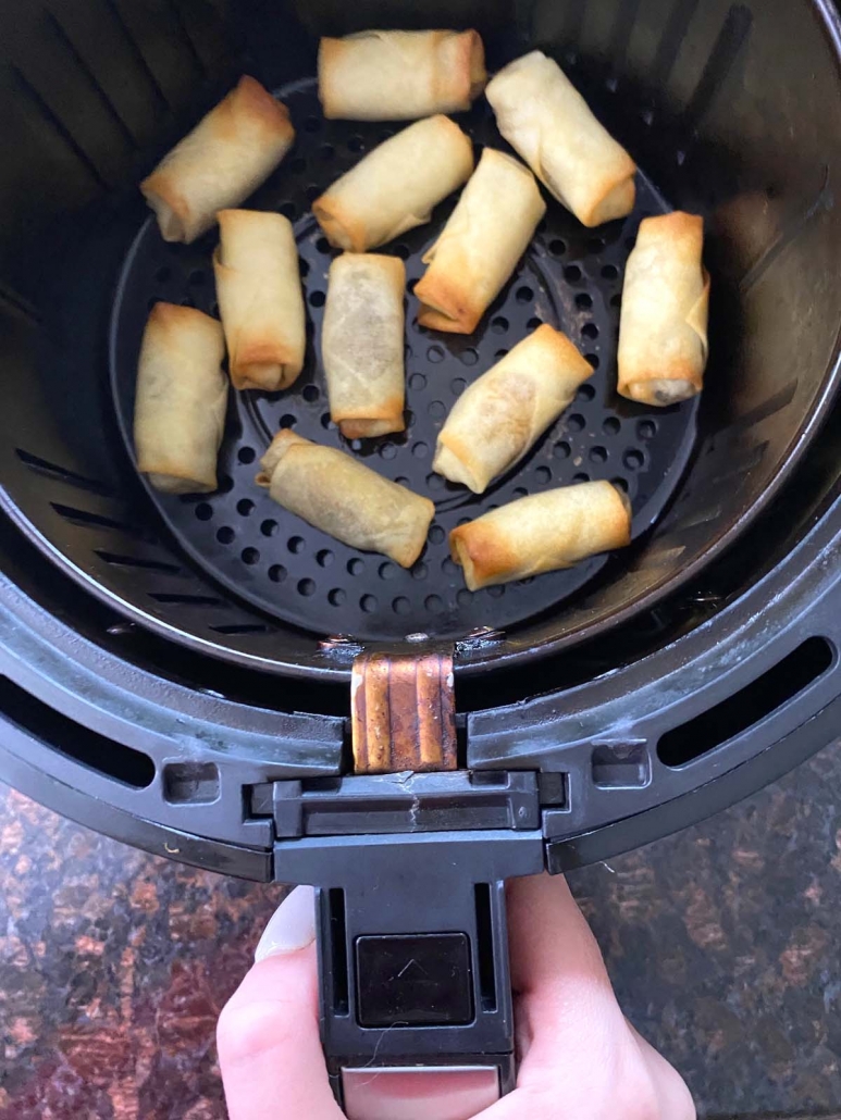 hand holding air fryer basket with spring rolls cooking inside