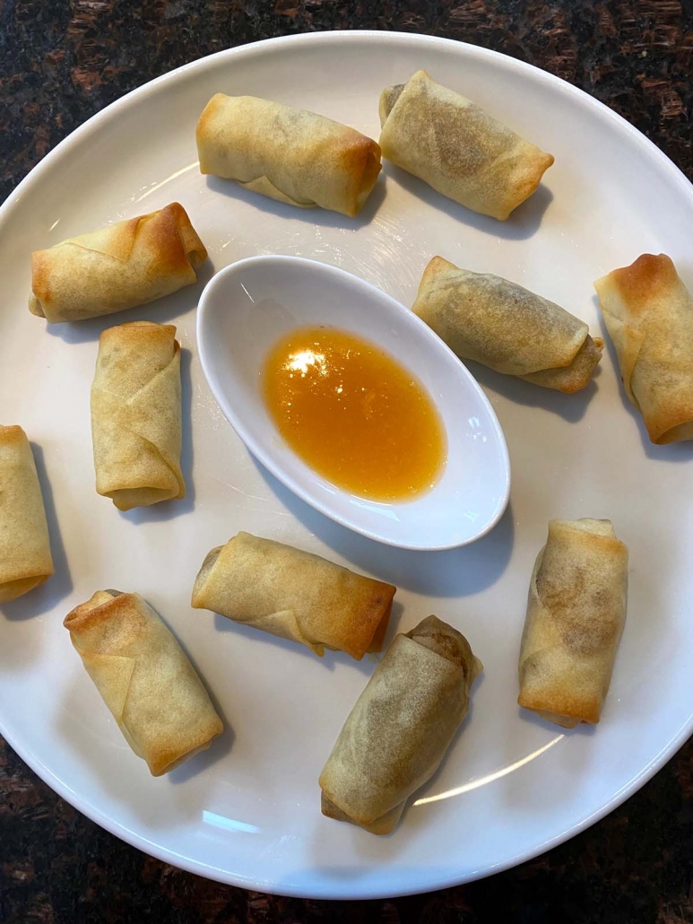 cooked spring rolls on a plate with dipping sauce in center