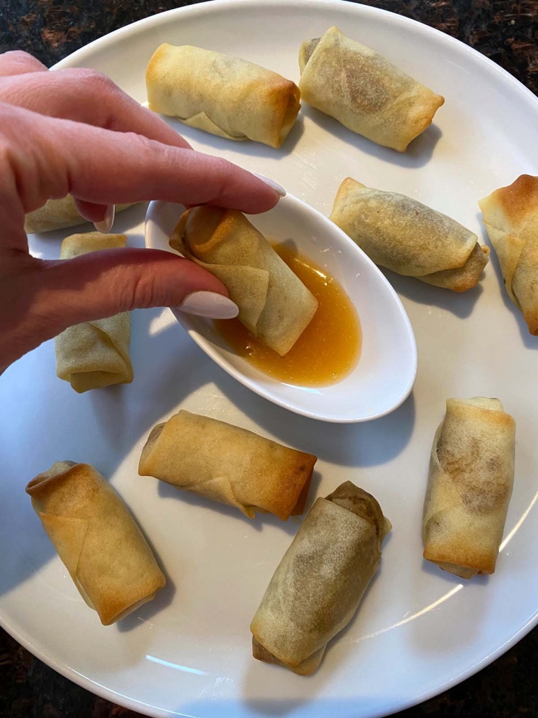 hand holding spring roll dipping in sauce