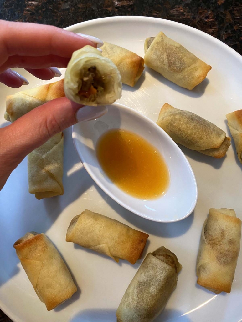hand holding partial spring roll above dipping sauce and plate