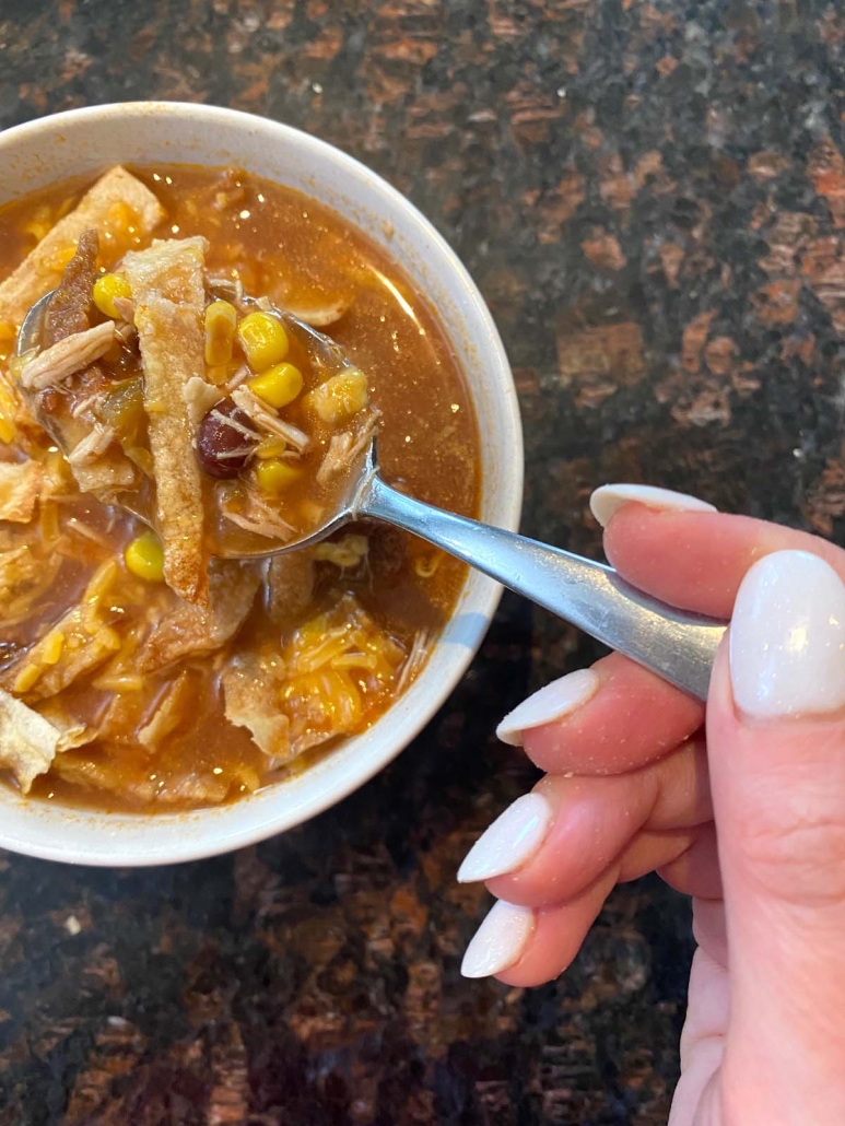 hand holding spoon with chicken tortilla soup in bowl