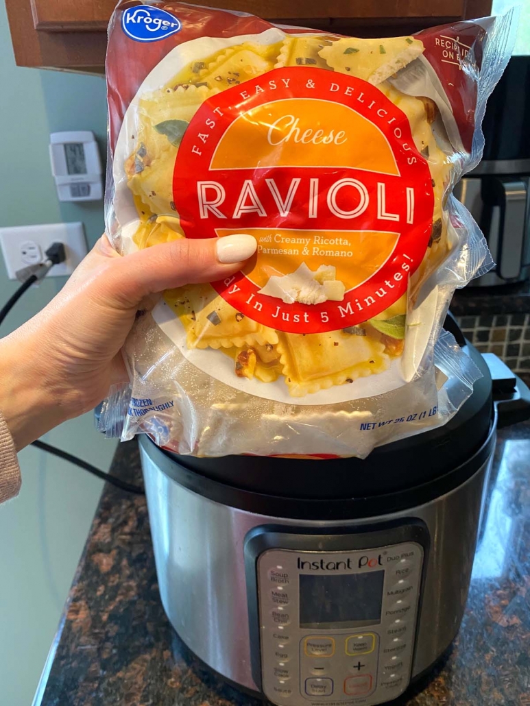 hand holding package of uncooked ravioli in front of instant pot