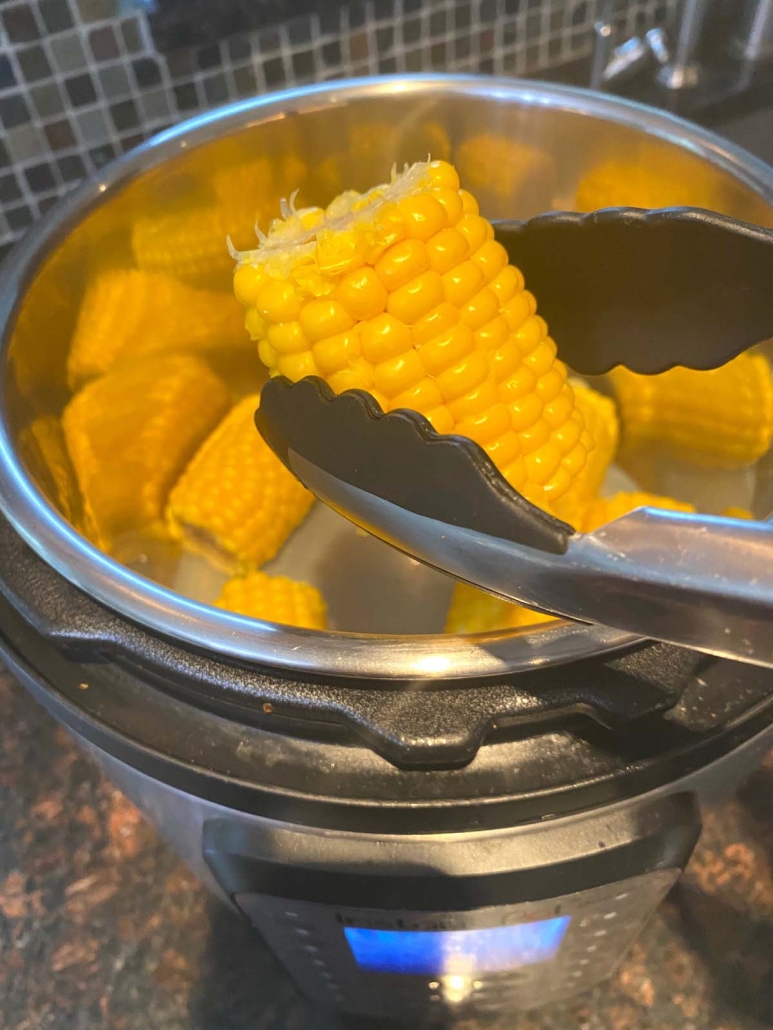 tongs holding corn on the cob piece above instant pot