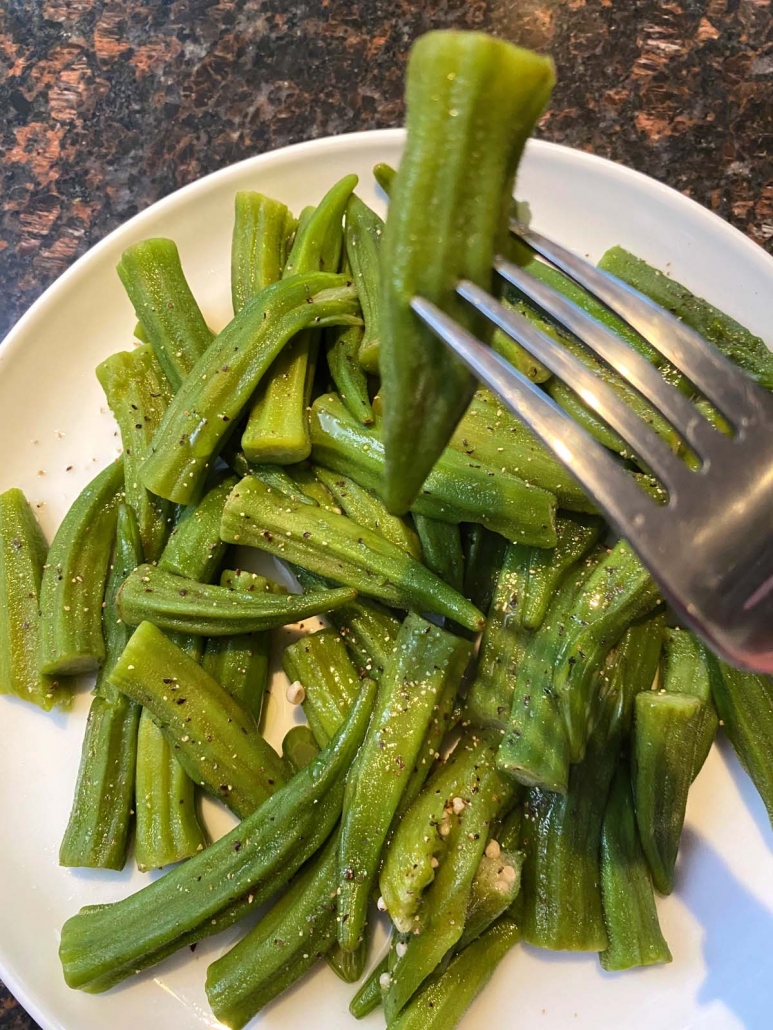 fork holding piece of okra over plate filled with okra