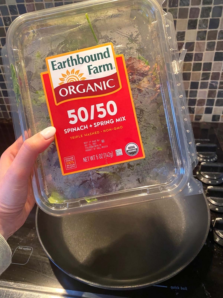 container of organic lettuce mix held in front of pan