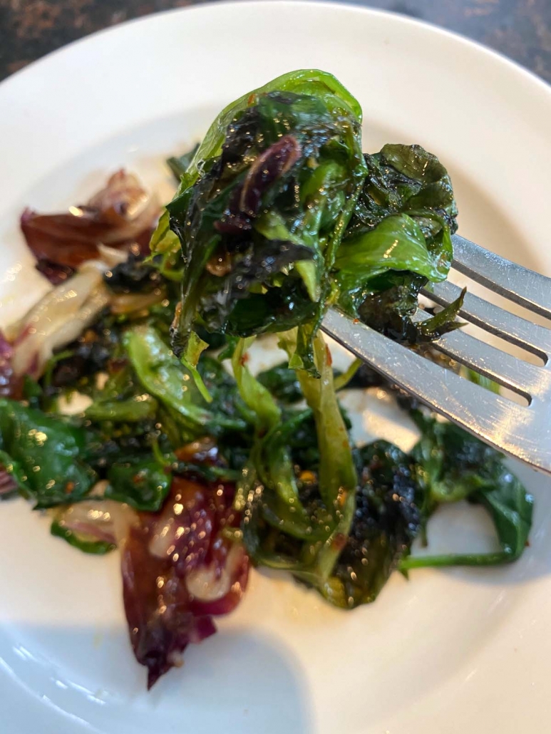 close up of fork holding sauteed lettuce on plate