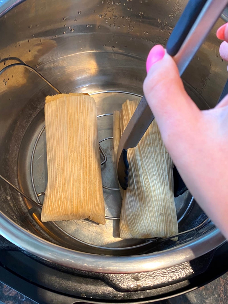 tamales being removed with a tong from the instant pot